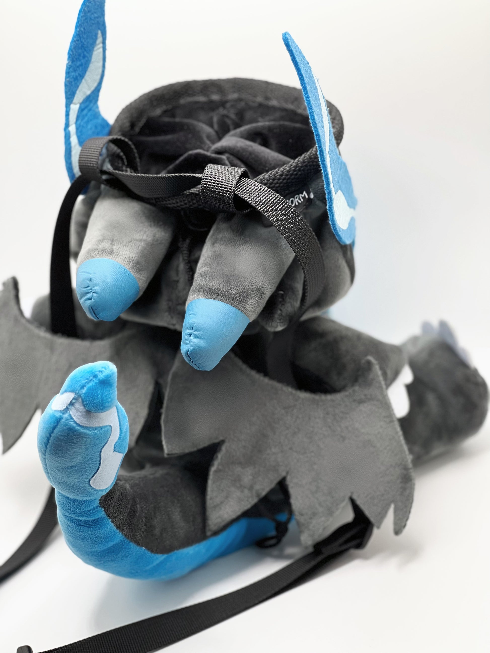 Handmade matte black plush climbing chalk bag shaped like a powerful dragon with bright electric blue wings and belly. Features small blue flame-like horns and aggressive embroidered eyes. Professional bouldering gear with a reinforced black rim, secure drawstring, and deep blue fleece lining.