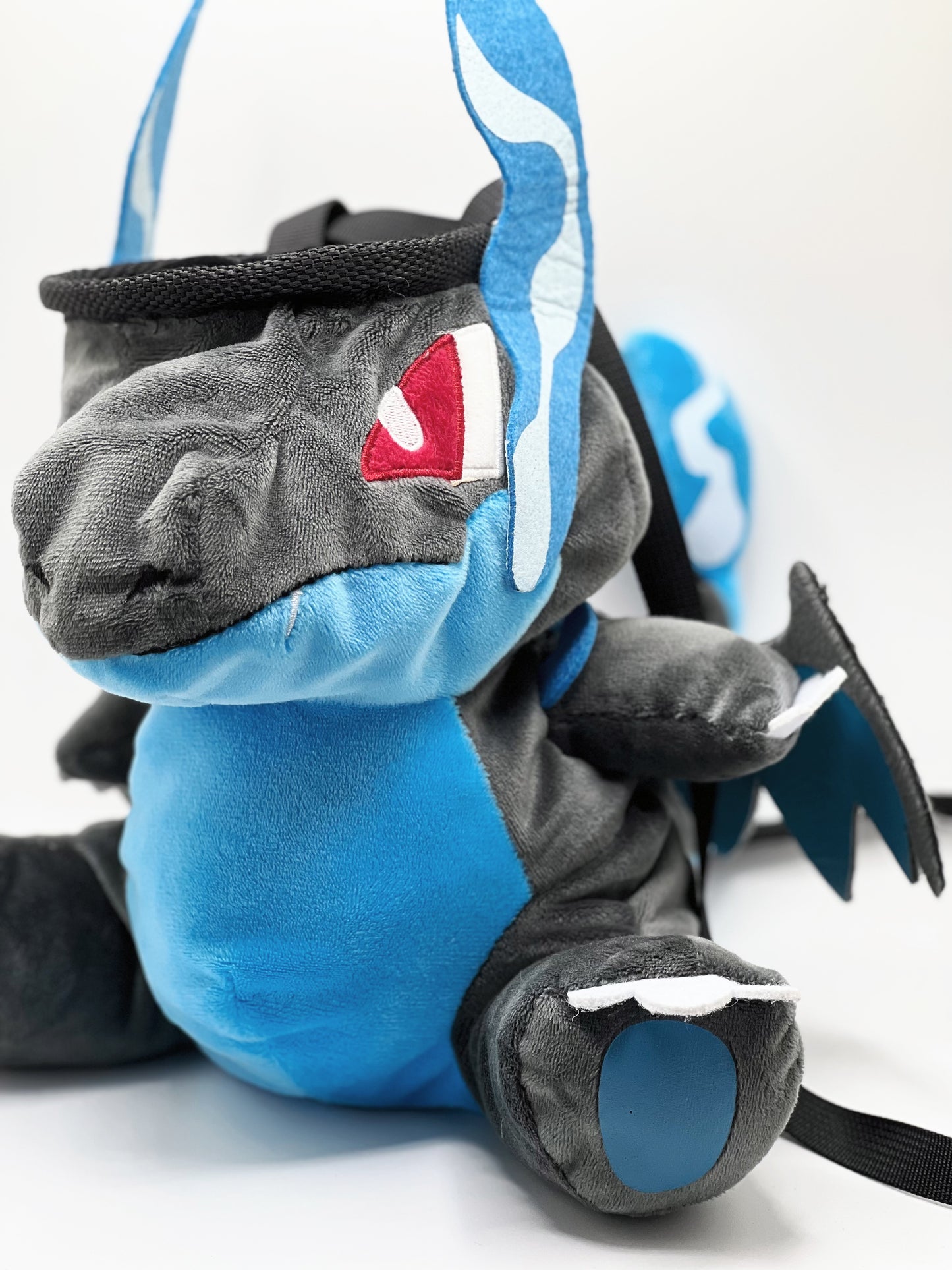 Handmade matte black plush climbing chalk bag shaped like a powerful dragon with bright electric blue wings and belly. Features small blue flame-like horns and aggressive embroidered eyes. Professional bouldering gear with a reinforced black rim, secure drawstring, and deep blue fleece lining.