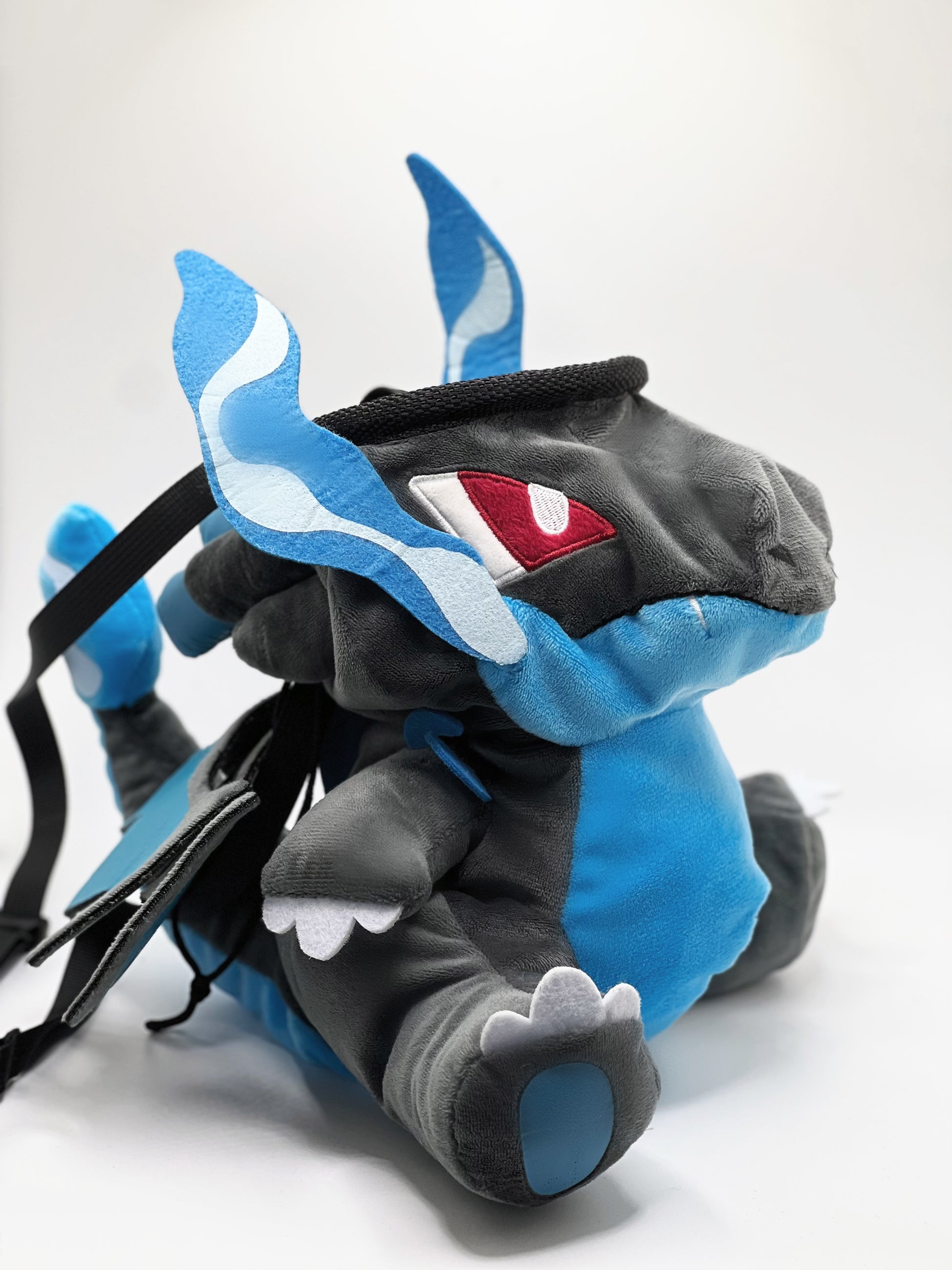 Handmade matte black plush climbing chalk bag shaped like a powerful dragon with bright electric blue wings and belly. Features small blue flame-like horns and aggressive embroidered eyes. Professional bouldering gear with a reinforced black rim, secure drawstring, and deep blue fleece lining.