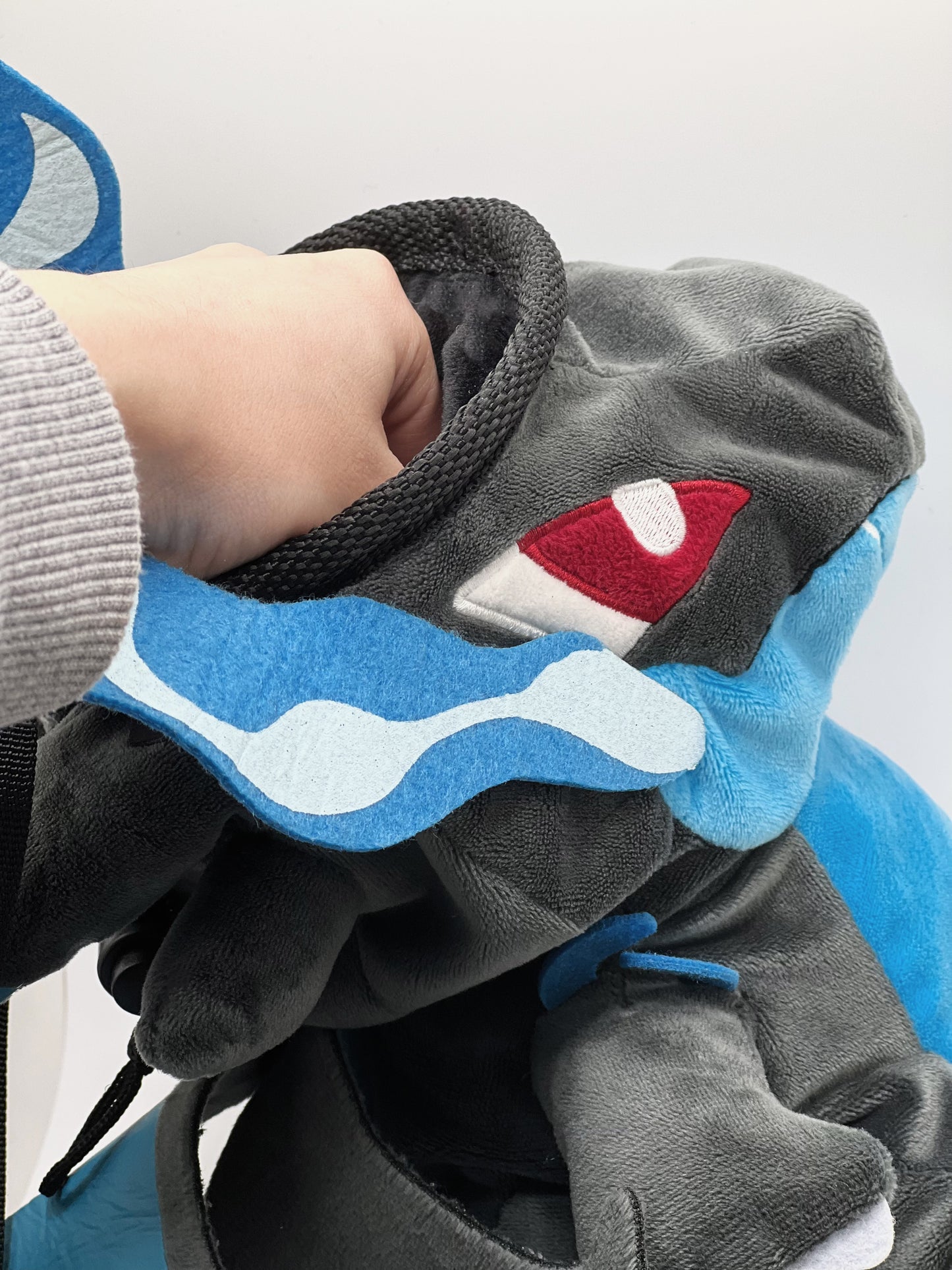 Handmade matte black plush climbing chalk bag shaped like a powerful dragon with bright electric blue wings and belly. Features small blue flame-like horns and aggressive embroidered eyes. Professional bouldering gear with a reinforced black rim, secure drawstring, and deep blue fleece lining.