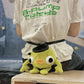 Soft plush climbing chalk bag shaped like a green game mascot with embroidered eyes. Inspired by the character Bing Bong from the co-op climbing video game PEAK. Handmade climbing chalk bag for bouldering and gym use by Fatworm