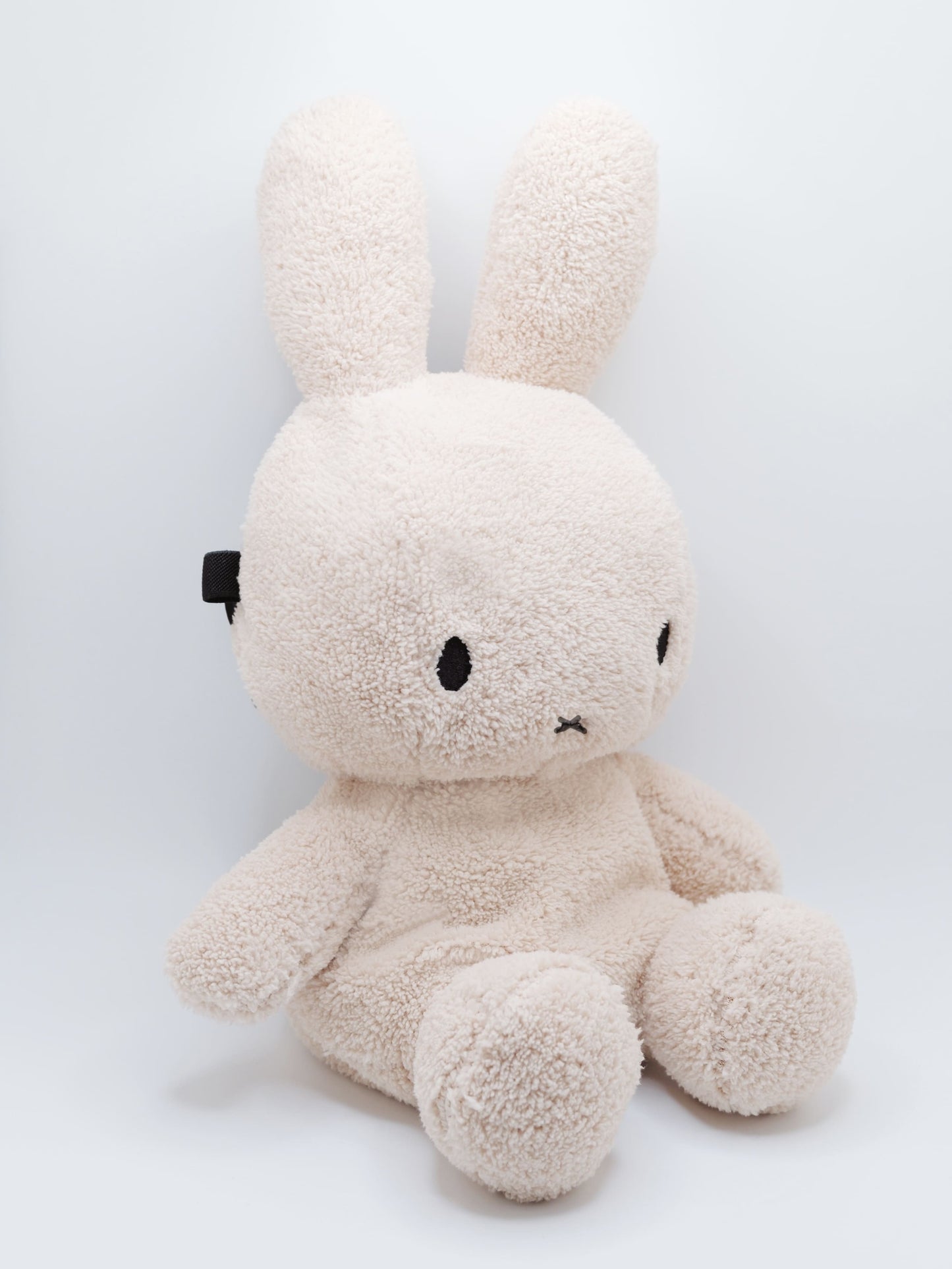 Handmade cream-colored Milk Tea Bunny plush climbing chalk bag with long floppy ears. Cute bouldering gift featuring a reinforced 12cm rim, secure drawstring, and deep black fleece lining. High-performance bouldering gear by Fatworm.