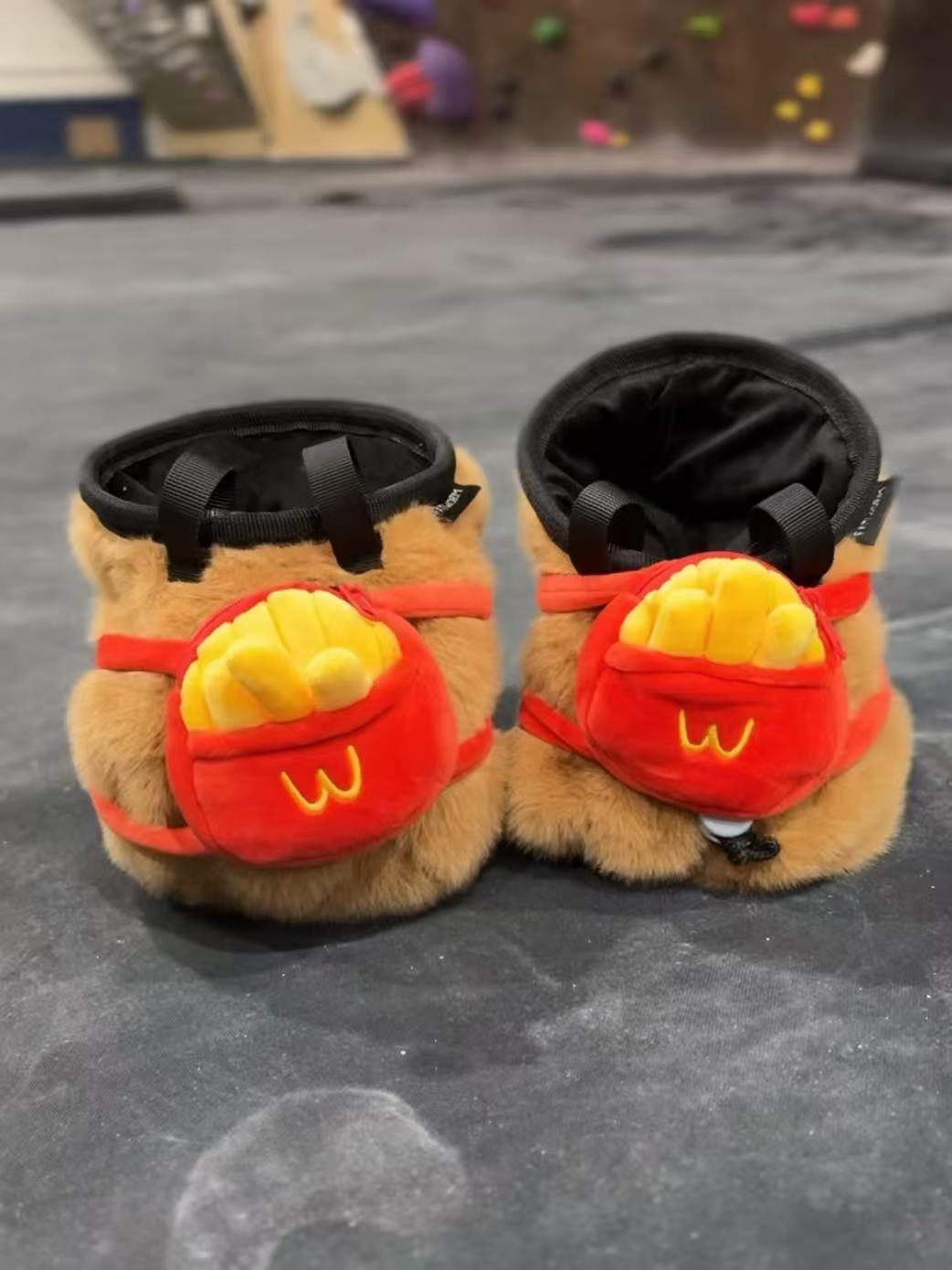 Handmade brown plush capybara climbing chalk bag wearing a red M backpack with removable plush fries. Unique bouldering gift featuring a reinforced 12cm rim and deep black fleece lining. Cute and funny bouldering gear by Fatworm.