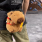 Handmade brown plush capybara climbing chalk bag wearing a red M backpack with removable plush fries. Unique bouldering gift featuring a reinforced 12cm rim and deep black fleece lining. Cute and funny bouldering gear by Fatworm.