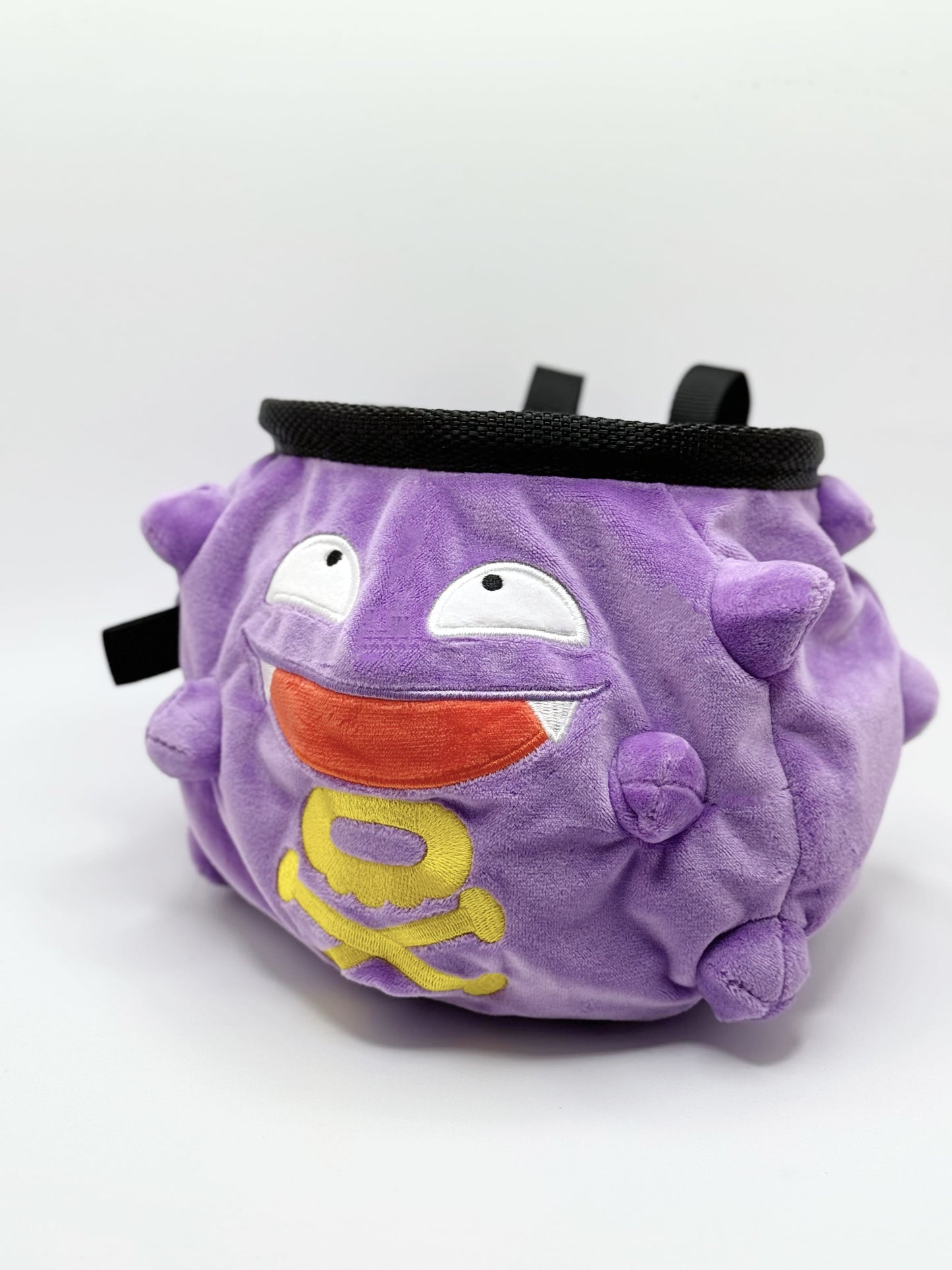 A cute anime plush chalk bag designed like Koffing by Fatworm. This functional purple bouldering and climbing accessory is handmade with a soft exterior, secure drawstring, and brush loop, making it perfect for rock climbing and a great gear addition for any climber.