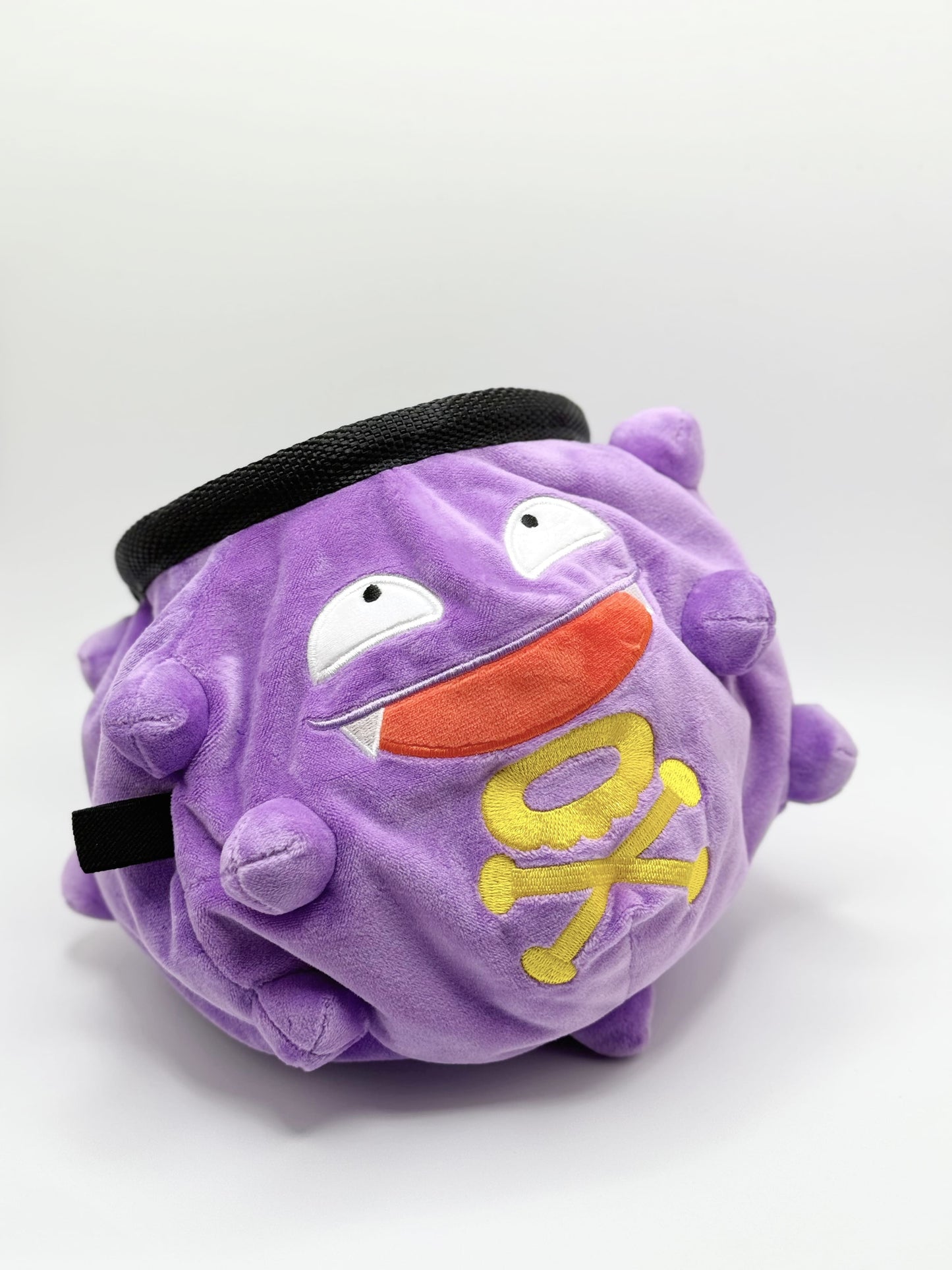 A cute anime plush chalk bag designed like Koffing by Fatworm. This functional purple bouldering and climbing accessory is handmade with a soft exterior, secure drawstring, and brush loop, making it perfect for rock climbing and a great gear addition for any climber.