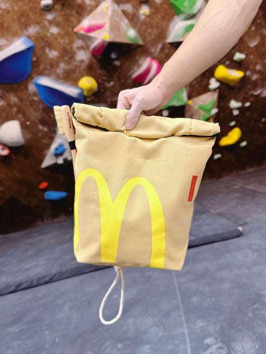 A cute plush bouldering chalk bucket by FATWORM featuring a classic red and yellow fast-food design. This functional and spacious ground-use accessory is handmade for bouldering and climbing for rock climbing, offering a long-durable design that makes the perfect climbing gift for a climber.