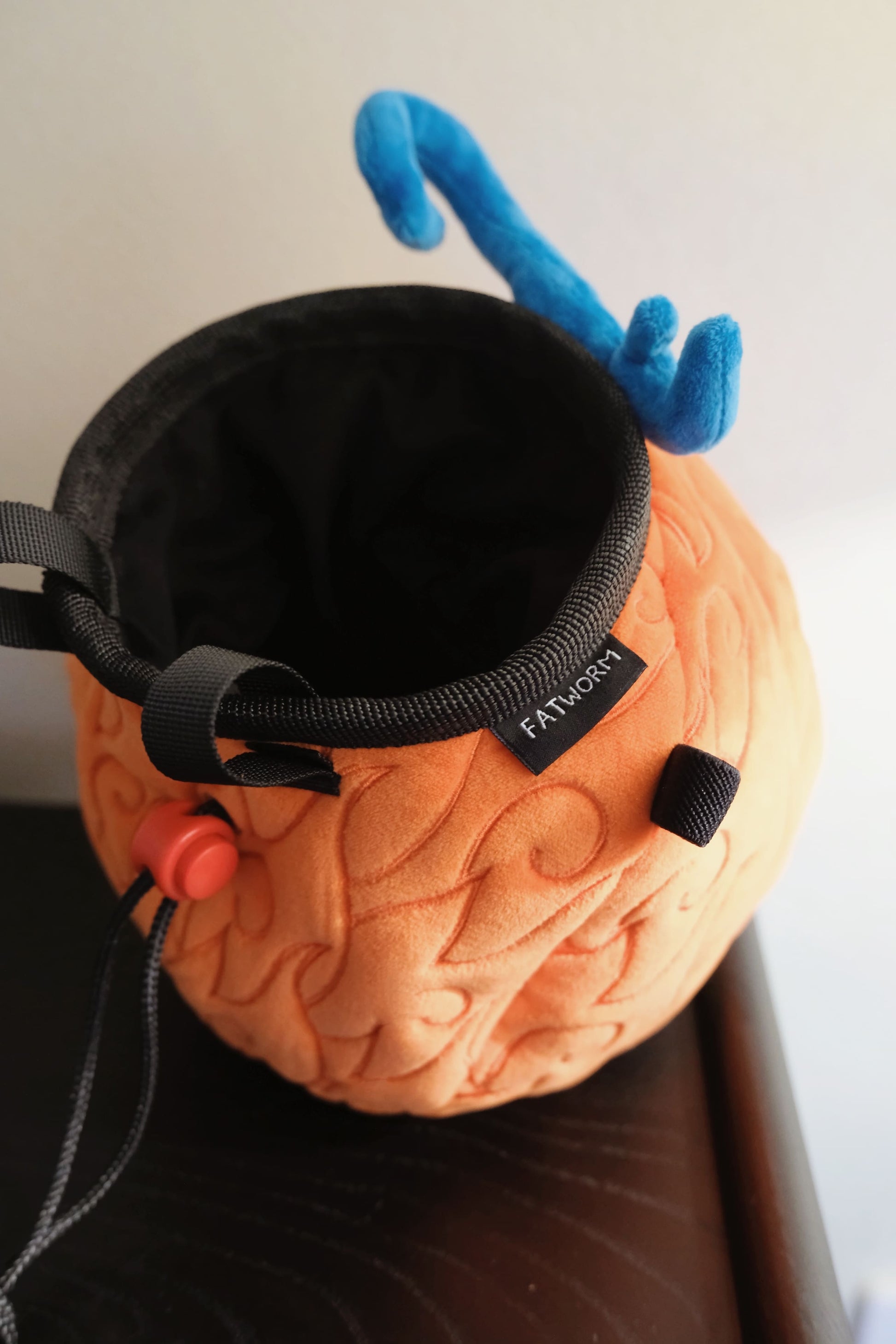 A cute anime plush chalk bag by FATWORM featuring an orange magical fire fruit with swirling flame patterns and a green stem, inspired by the fiery hero Ace. This functional and fluffy bouldering accessory is handmade for bouldering and climbing for rock climbing, offering a long-durable design that makes the perfect climbing gift for a climber.
