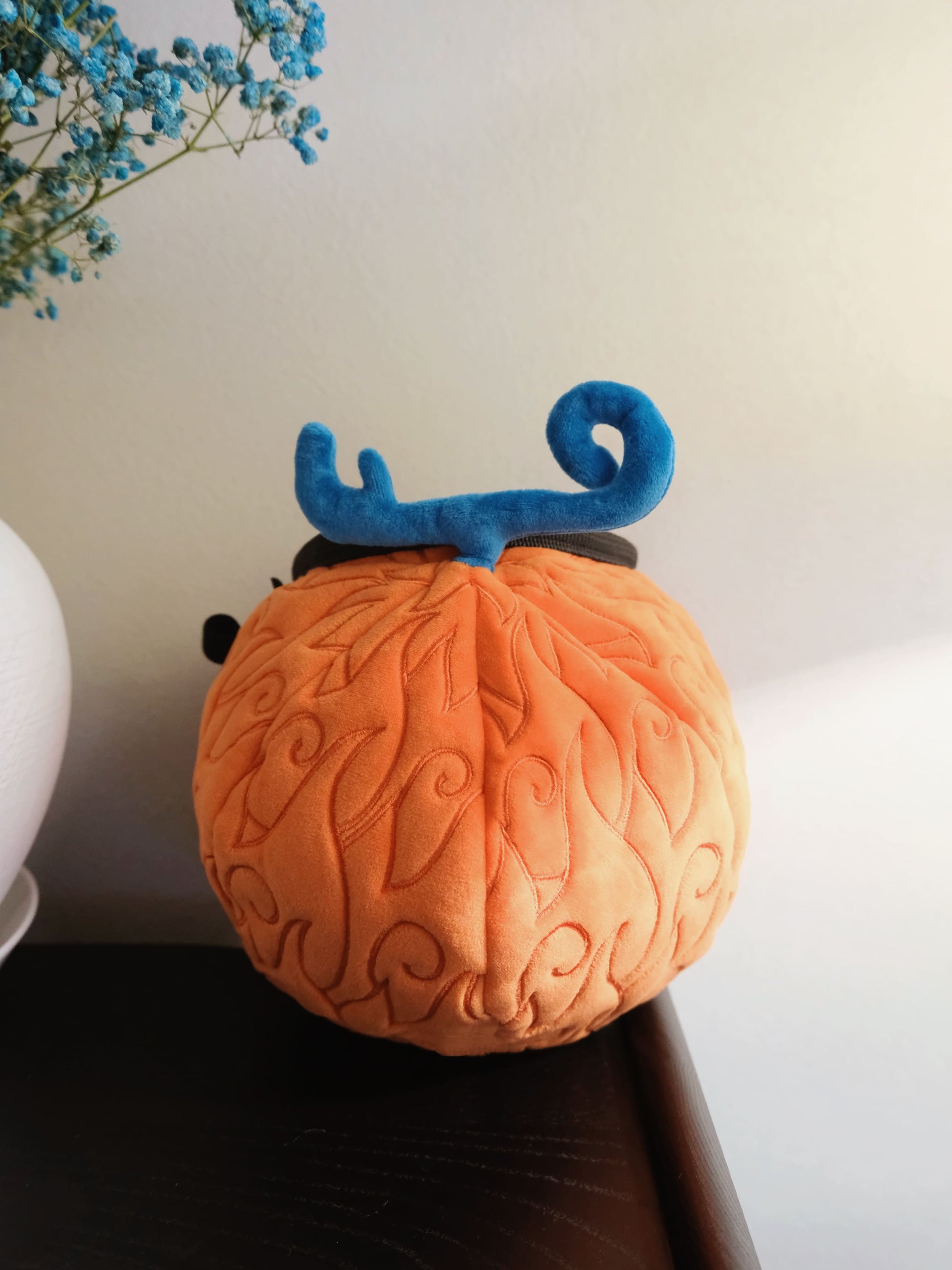 A cute anime plush chalk bag by FATWORM featuring an orange magical fire fruit with swirling flame patterns and a green stem, inspired by the fiery hero Ace. This functional and fluffy bouldering accessory is handmade for bouldering and climbing for rock climbing, offering a long-durable design that makes the perfect climbing gift for a climber.