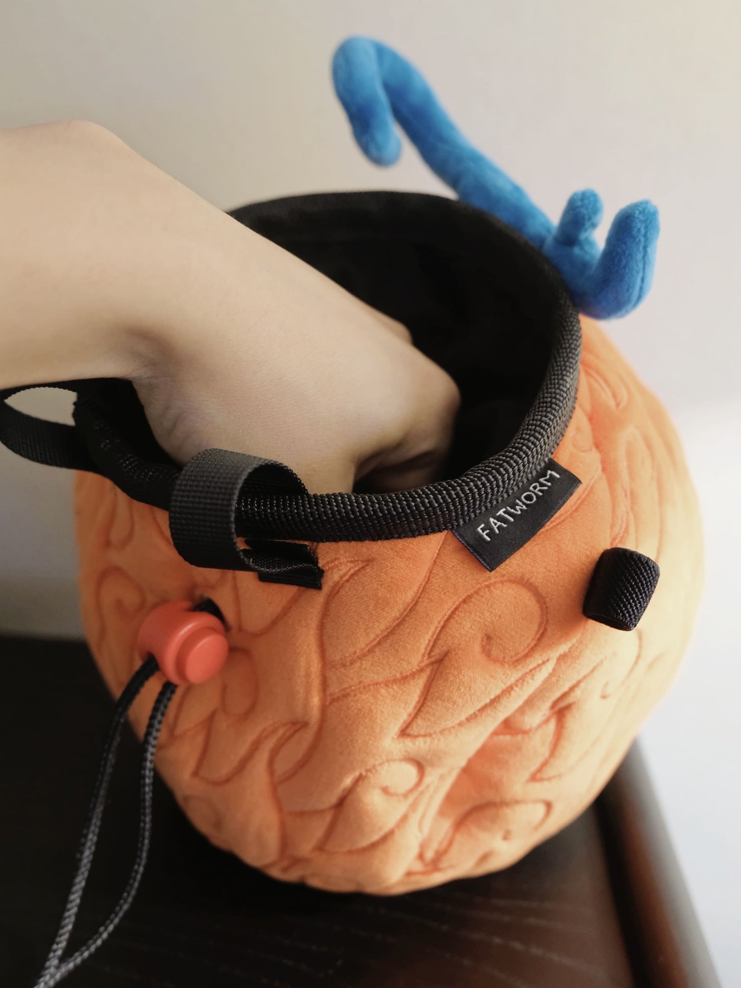 A cute anime plush chalk bag by FATWORM featuring an orange magical fire fruit with swirling flame patterns and a green stem, inspired by the fiery hero Ace. This functional and fluffy bouldering accessory is handmade for bouldering and climbing for rock climbing, offering a long-durable design that makes the perfect climbing gift for a climber.
