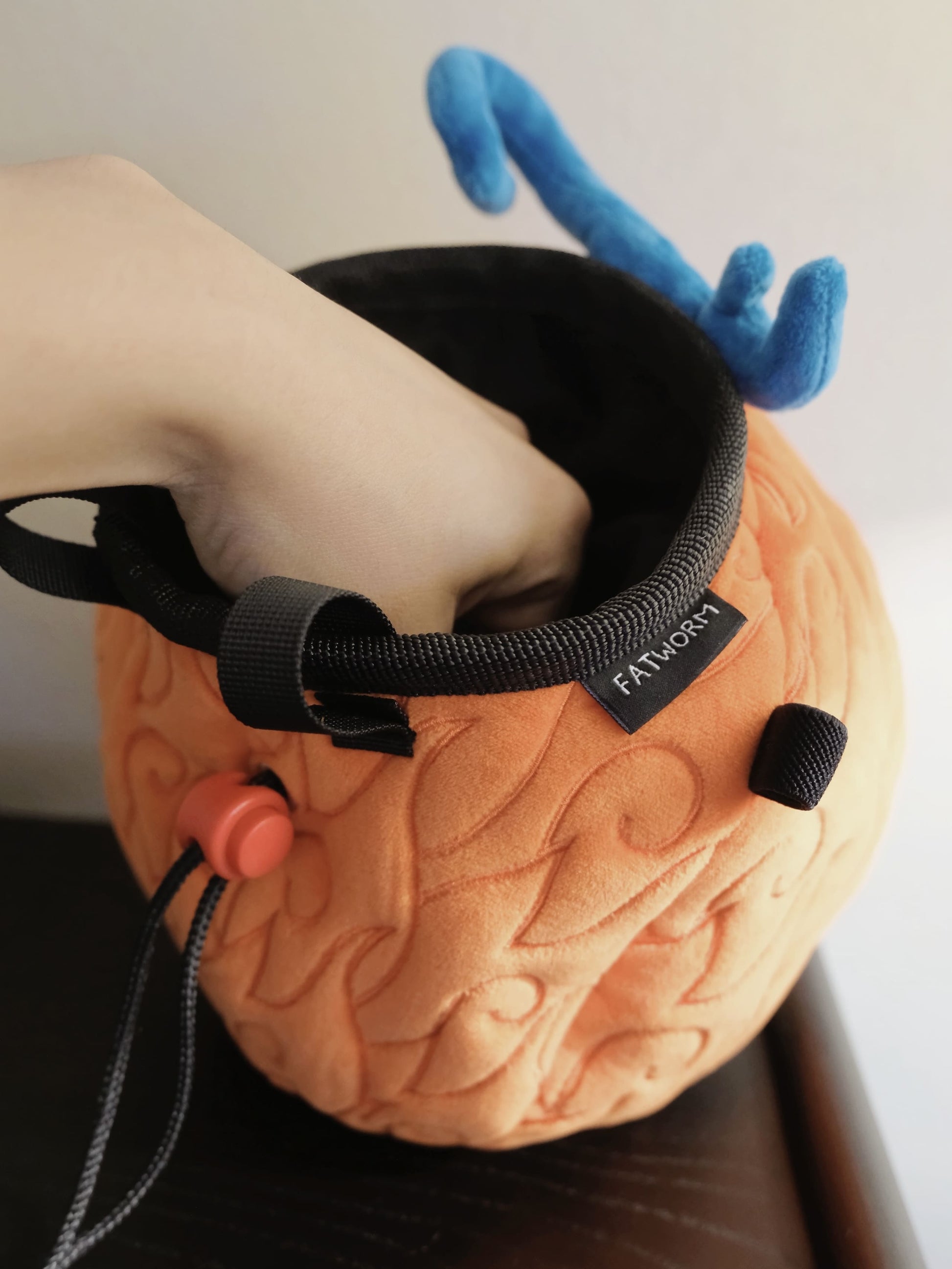 A cute anime plush chalk bag by FATWORM featuring an orange magical fire fruit with swirling flame patterns and a green stem, inspired by the fiery hero Ace. This functional and fluffy bouldering accessory is handmade for bouldering and climbing for rock climbing, offering a long-durable design that makes the perfect climbing gift for a climber.