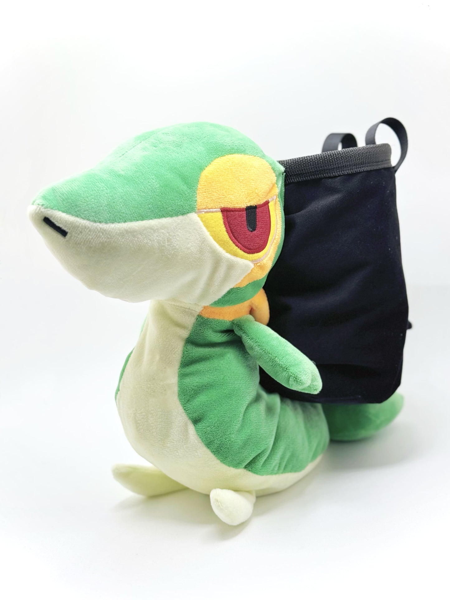 A cute, handmade plush climbing chalk bag designed to look like the Snivy, featuring a sleek green and cream body with yellow leaf-like accents and large, confident eyes. Designed with high functionality by a climber, it includes a wide black rim opening at the top for easy chalk access. A great climbing gift for trainers who want to catch them all.