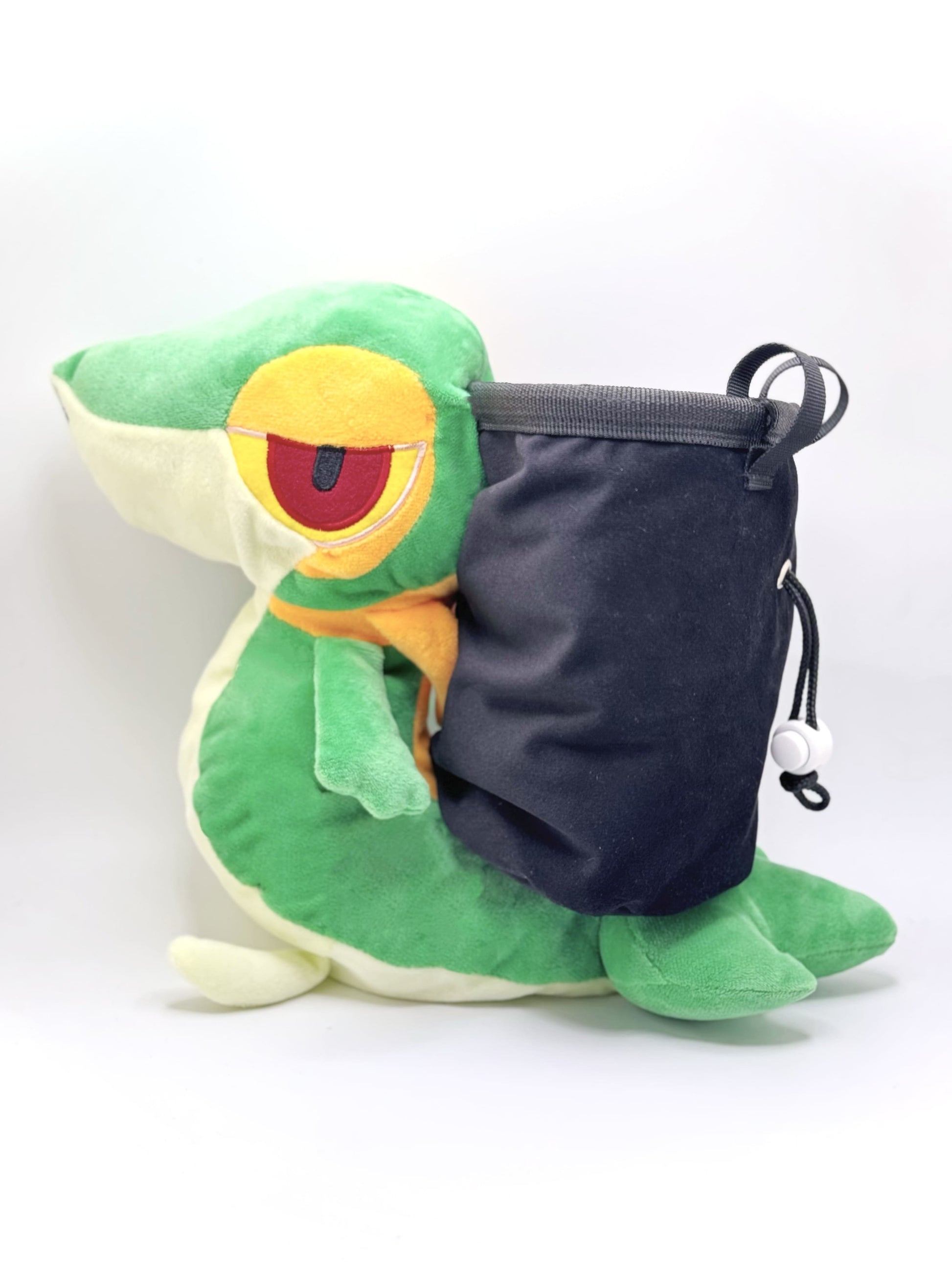 A cute, handmade plush climbing chalk bag designed to look like the Snivy, featuring a sleek green and cream body with yellow leaf-like accents and large, confident eyes. Designed with high functionality by a climber, it includes a wide black rim opening at the top for easy chalk access. A great climbing gift for trainers who want to catch them all.