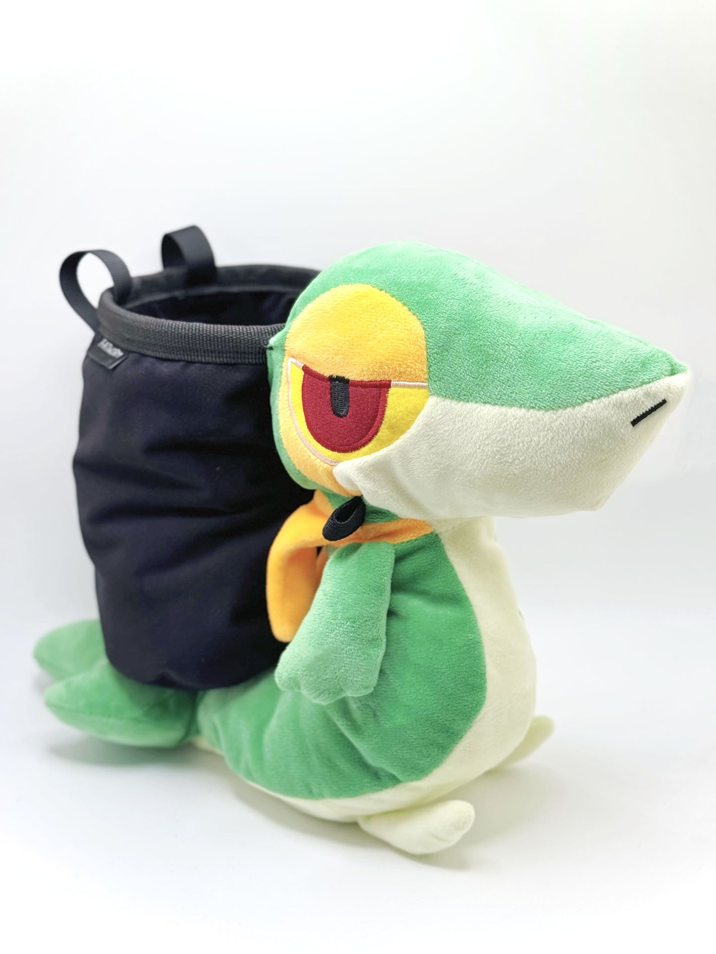 A cute, handmade plush climbing chalk bag designed to look like the Snivy, featuring a sleek green and cream body with yellow leaf-like accents and large, confident eyes. Designed with high functionality by a climber, it includes a wide black rim opening at the top for easy chalk access. A great climbing gift for trainers who want to catch them all.