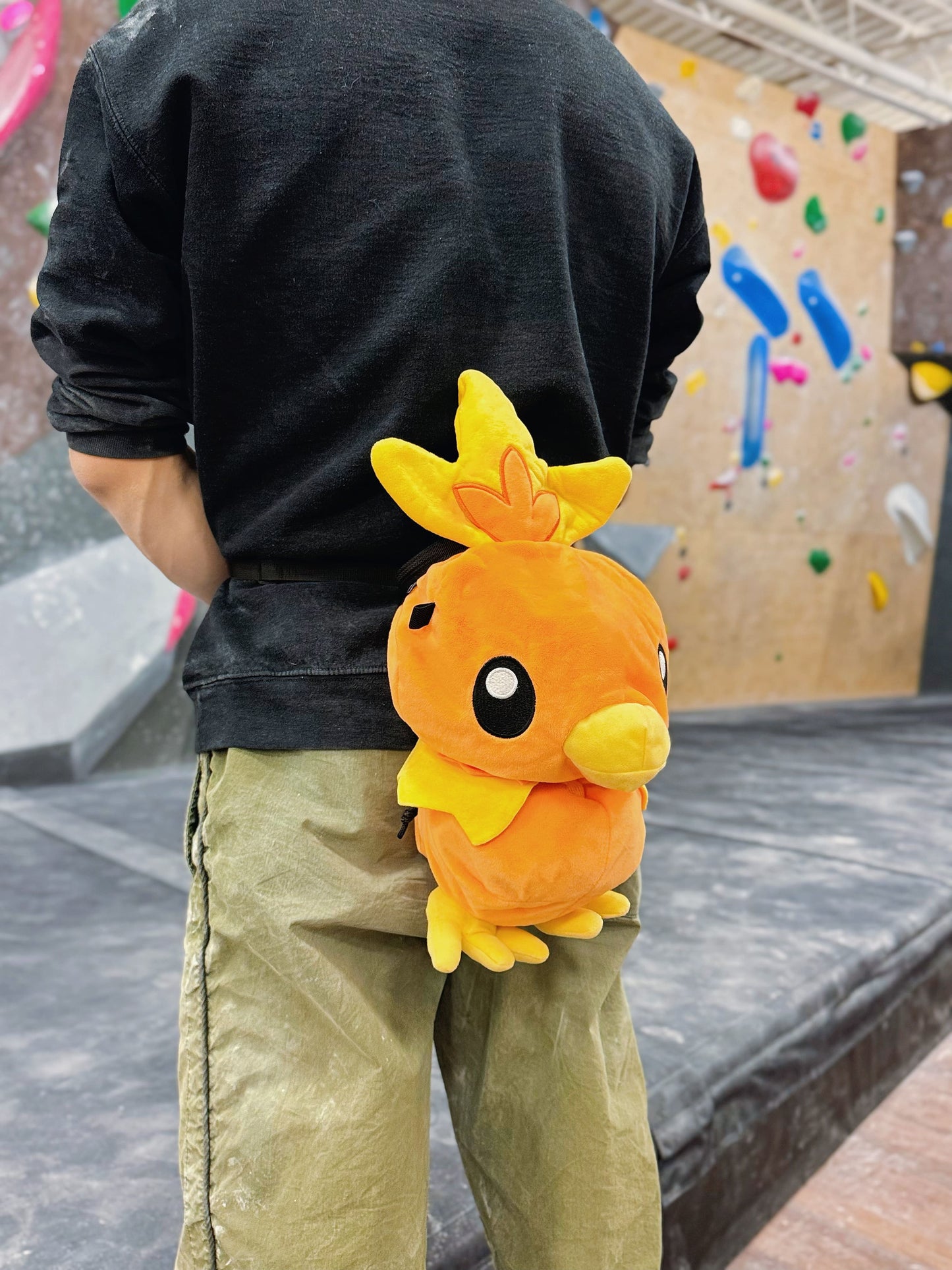 Handmade orange plush Torchic fire chick climbing chalk bag for bouldering. Features yellow feather tufts and a cute bird silhouette. High-quality plush bouldering gift with a 12cm reinforced rim, secure drawstring, and deep black fleece lining for rock climbing.