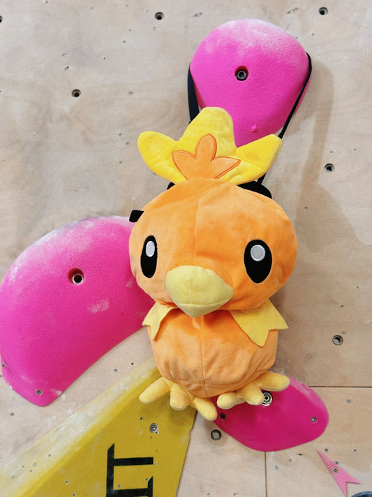 Handmade orange plush Torchic fire chick climbing chalk bag for bouldering. Features yellow feather tufts and a cute bird silhouette. High-quality plush bouldering gift with a 12cm reinforced rim, secure drawstring, and deep black fleece lining for rock climbing.